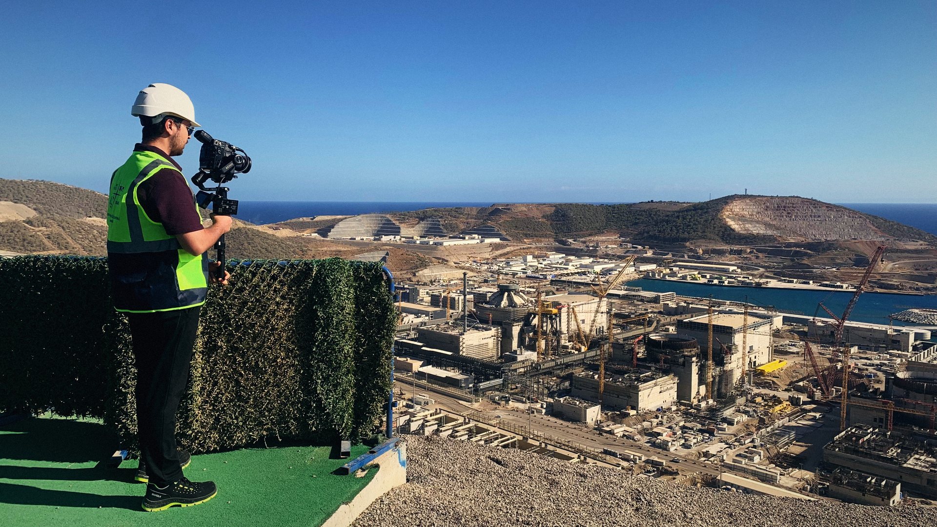 Camera operator on a gimbal overlooking the Akkuyu power plant site and the sea